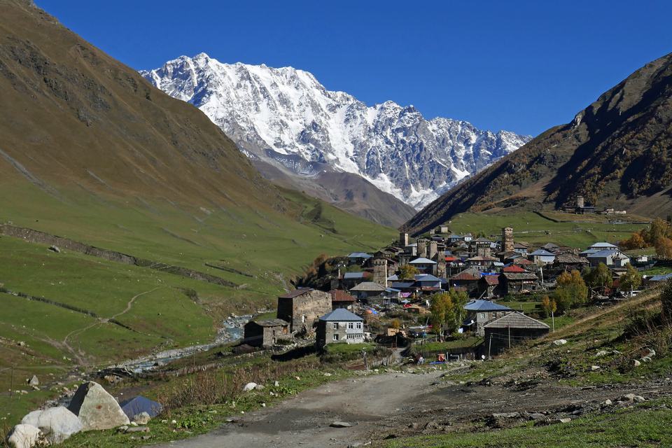 格鲁吉亚上斯瓦涅季的乌树故里村：秋天的山谷里是中世纪石砌塔楼和石板屋顶的村舍，背后是积雪的什哈拉峰，天空湛蓝无云