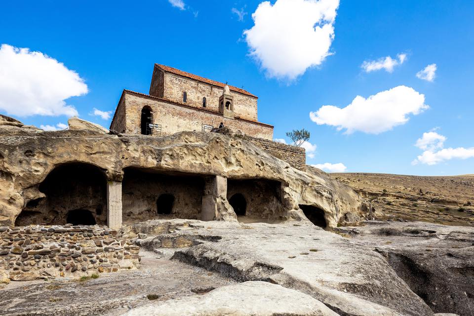 格鲁吉亚乌普利斯齐赫岩城：在山岩里凿出的厅堂，岩顶上立着一座红砖小教堂，深蓝的天空里飘着白云